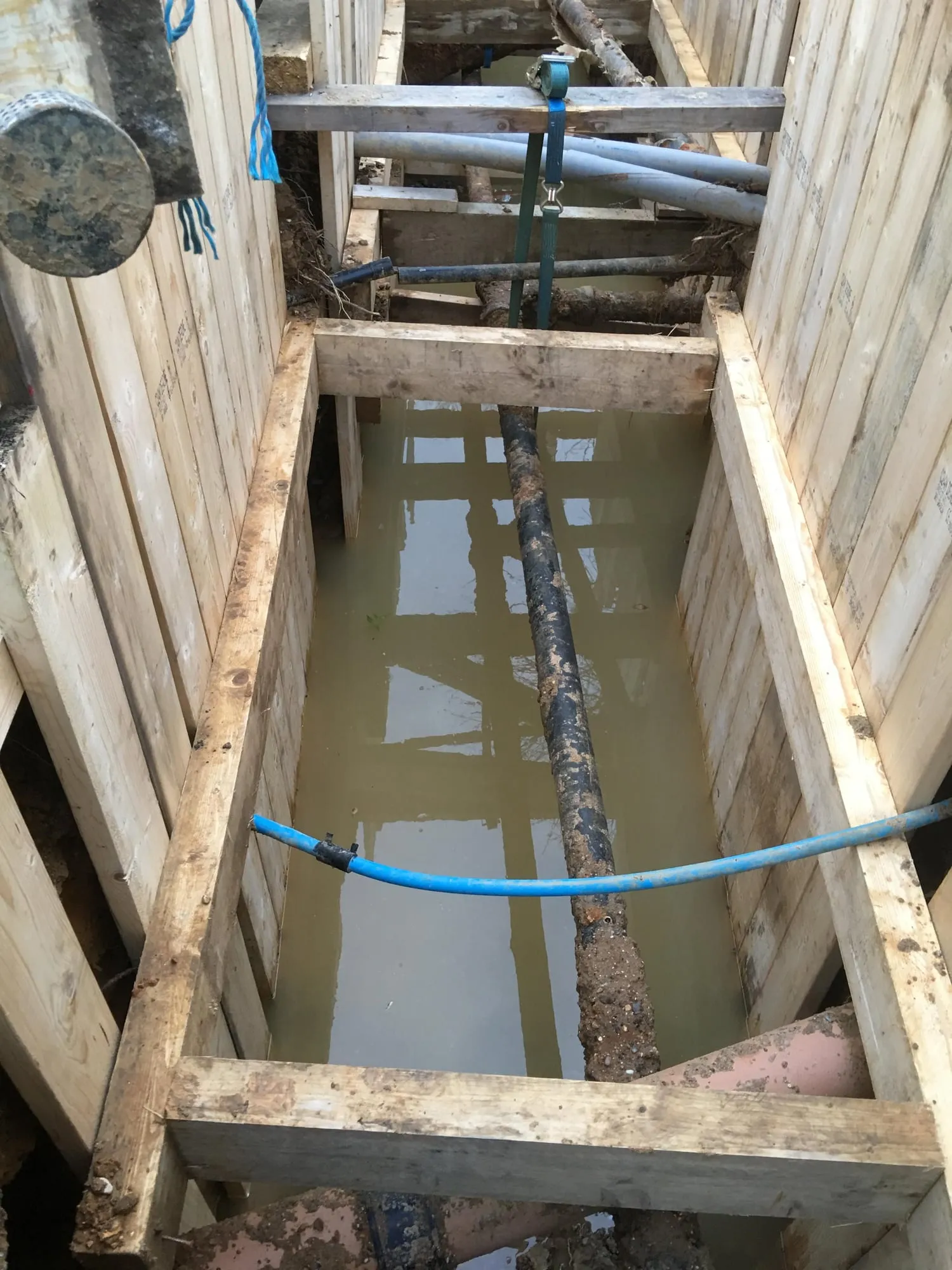 Timber trench support around a blue water pipe in a deep excavation